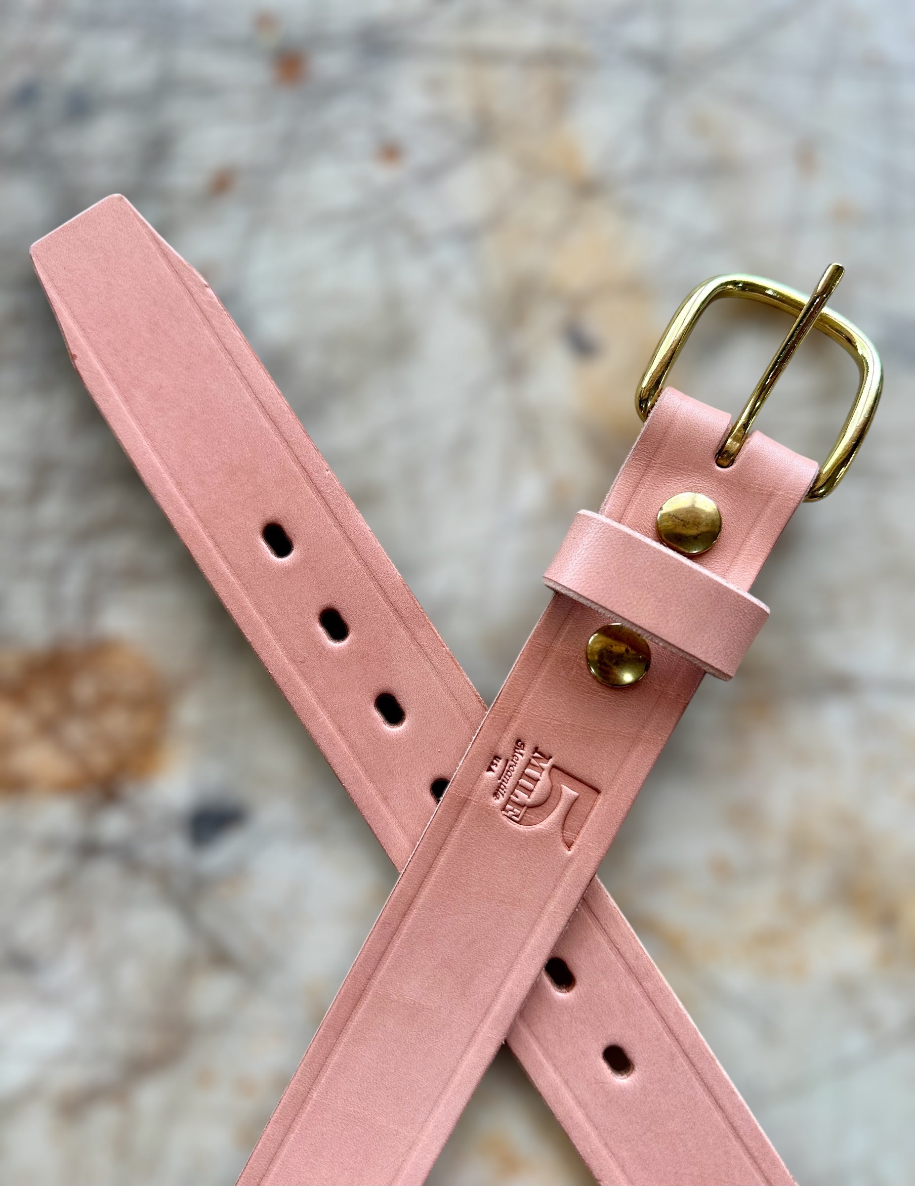 Pink leather belt with gold buckle on a textured surface