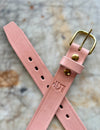 Pink leather belt with gold buckle on a textured surface