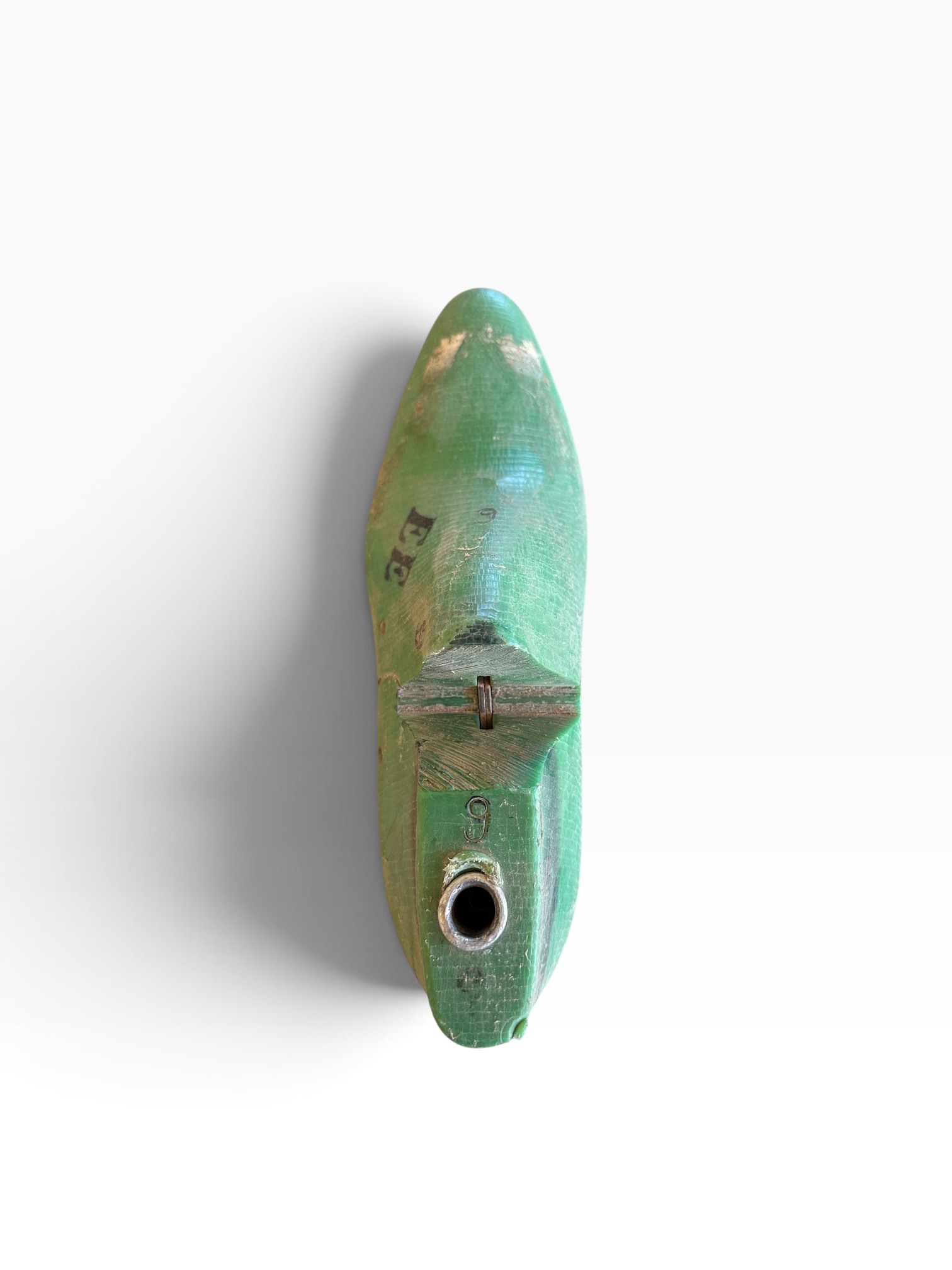 A small, vintage-style green metal object with a pointed top, weathered patina, and a circular hole near the bottom, photographed against a plain white background.
