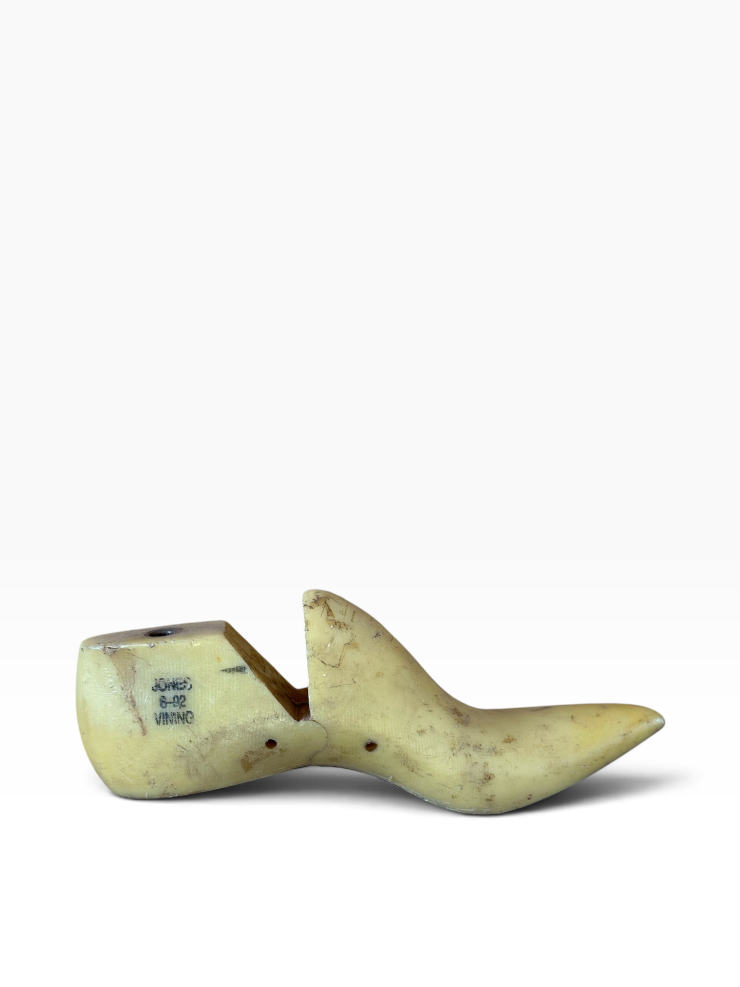 A single carved wooden shoe tree or foot mold shown on a plain white studio background. The item appears light tan to pale yellow wood with some darker brown grain and small dark markings on the left side.