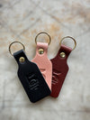 Three leather keychains in black, pink, and red on a textured surface.