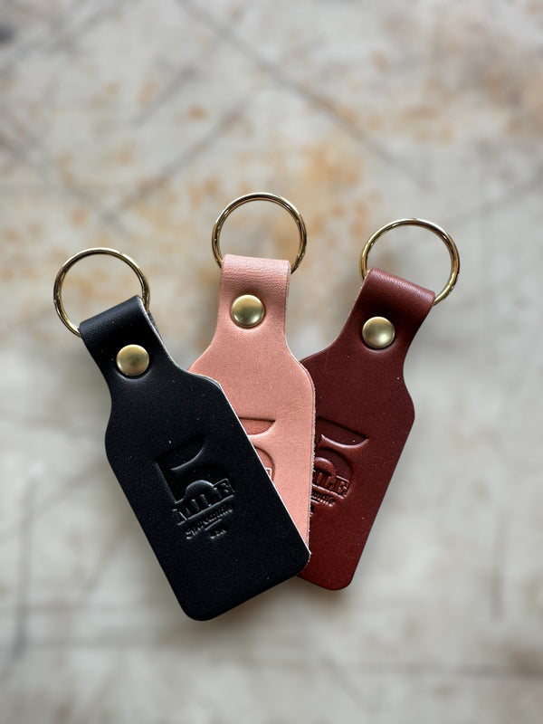 Three leather keychains in black, pink, and red on a textured surface.
