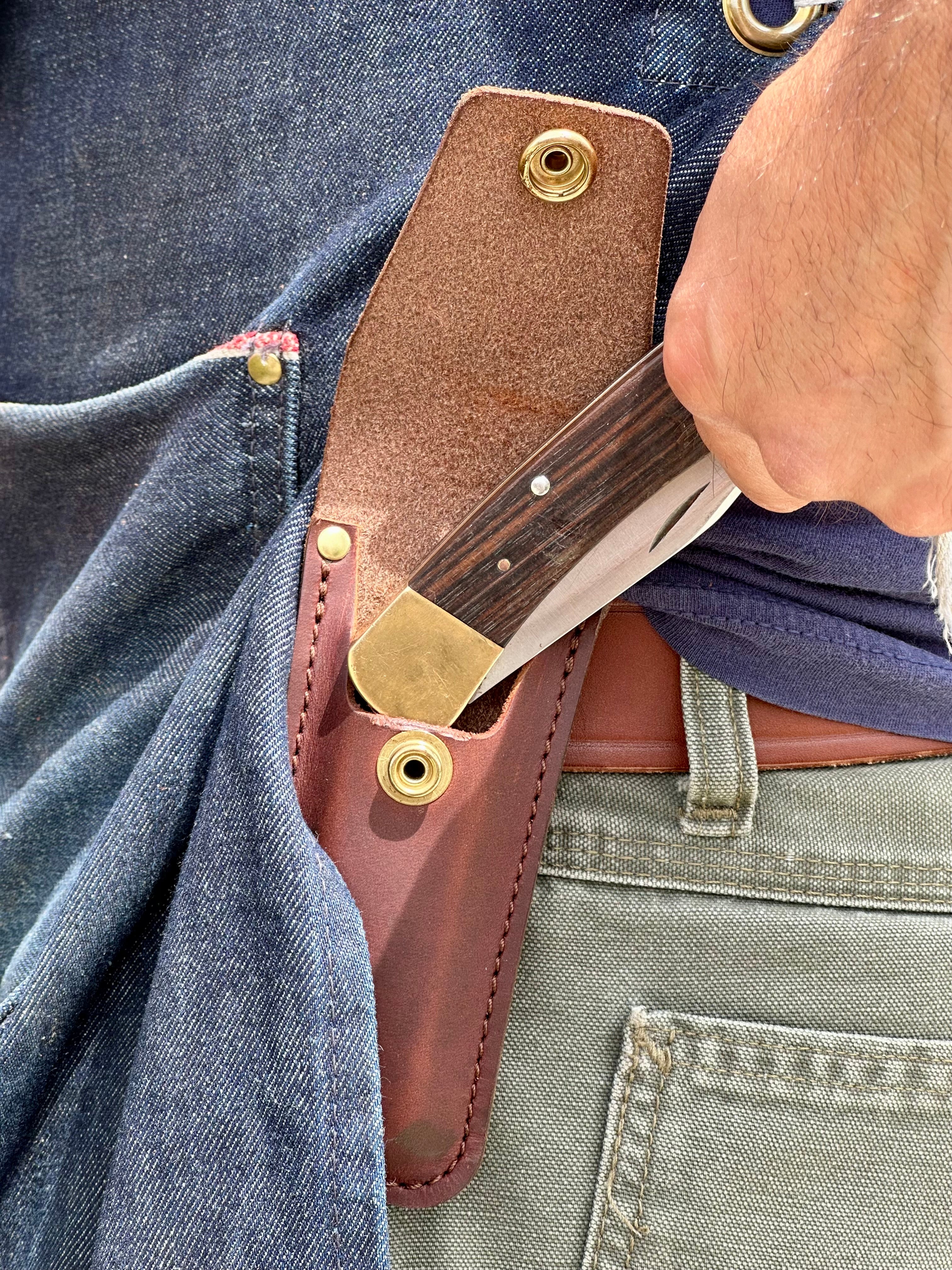 Knife sheath with a knife partially extracted from it, attached to a person's waistband.