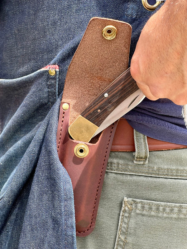 Knife sheath with a knife partially extracted from it, attached to a person's waistband.