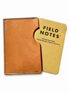 A tan leather pocket notebook cover holding a yellow Field Notes memo book, shown on a clean white background.