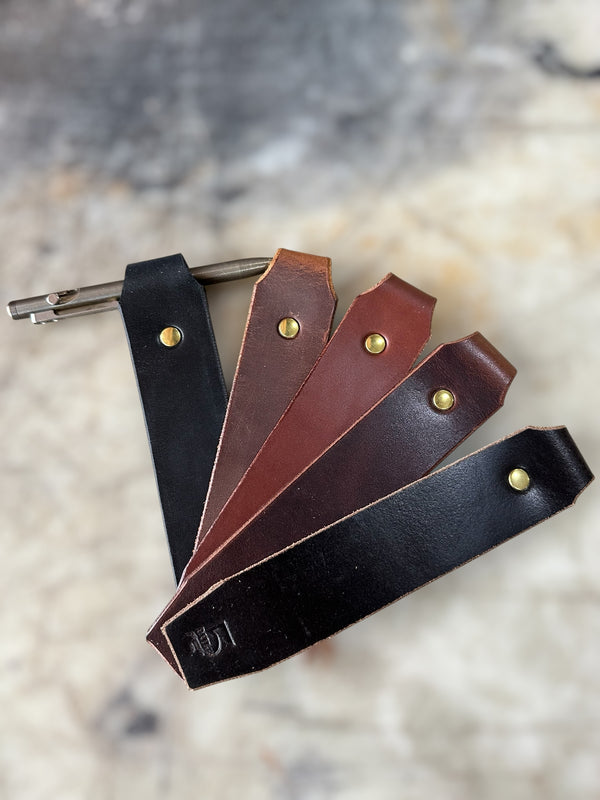 Set of leather keychains in black, brown, and dark brown on a textured surface.