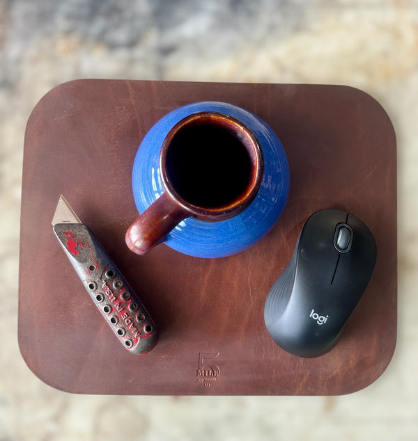 Blue mug, knife, and Logitech mouse on a brown leather tray.