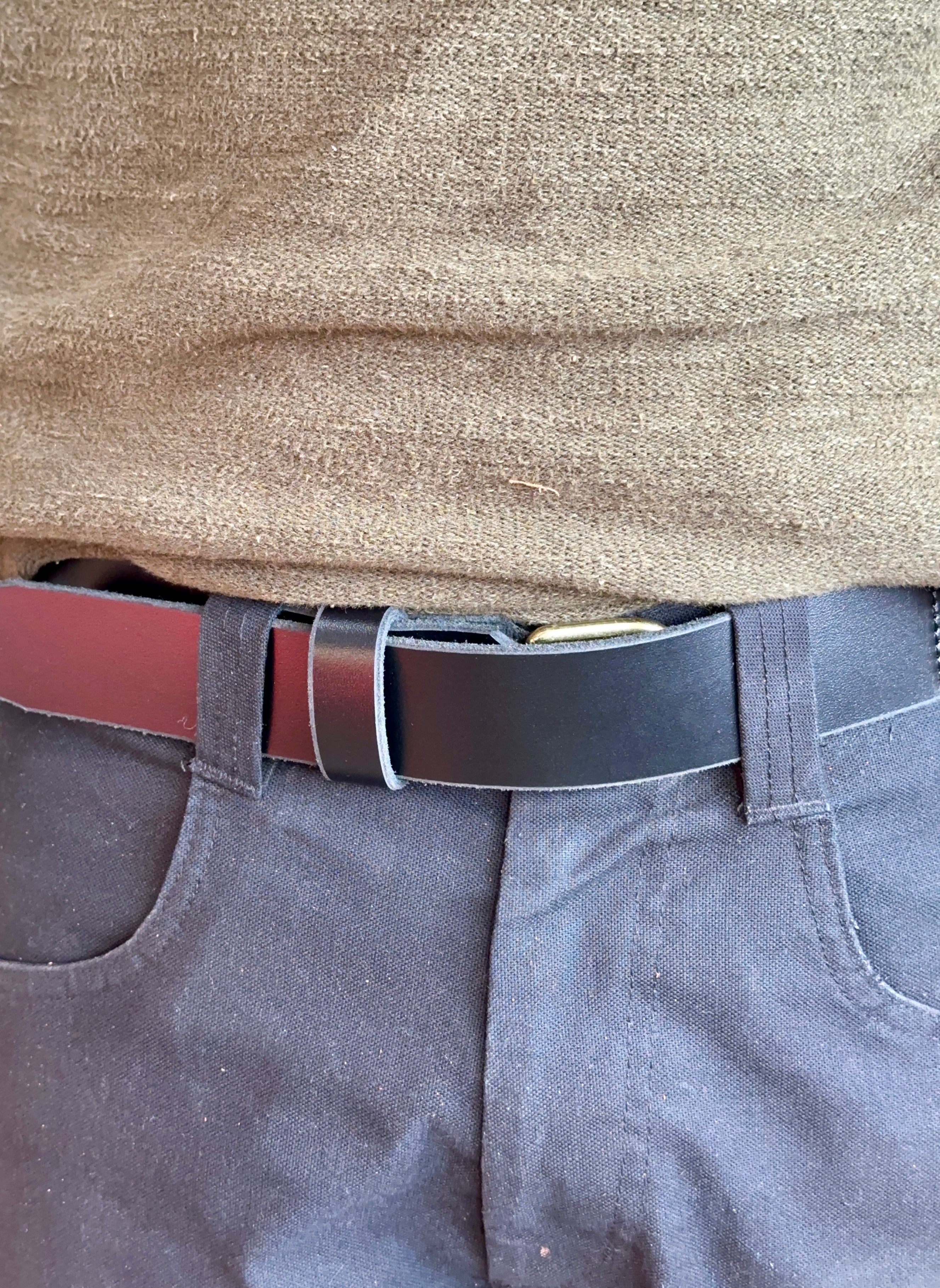 Close-up of a person wearing a black belt, green sweater, and grey pants