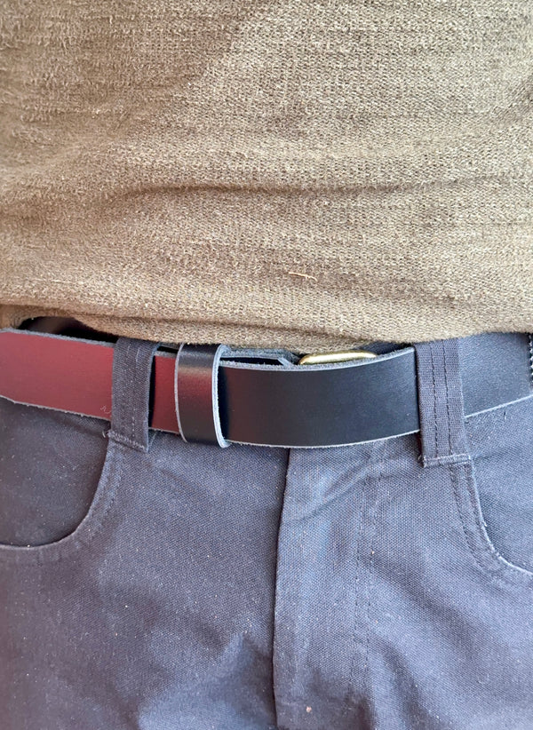Close-up of a person wearing a black belt, green sweater, and grey pants