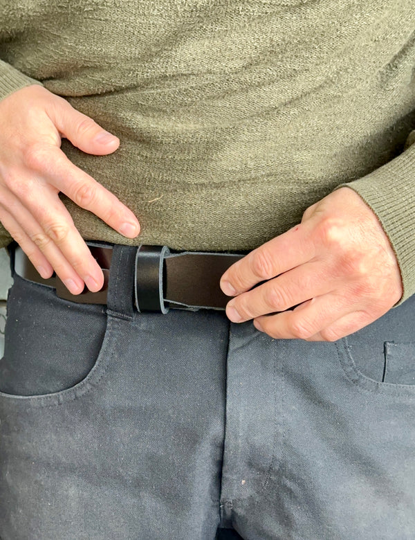 Person adjusting a black belt on gray pants with a green sweater.