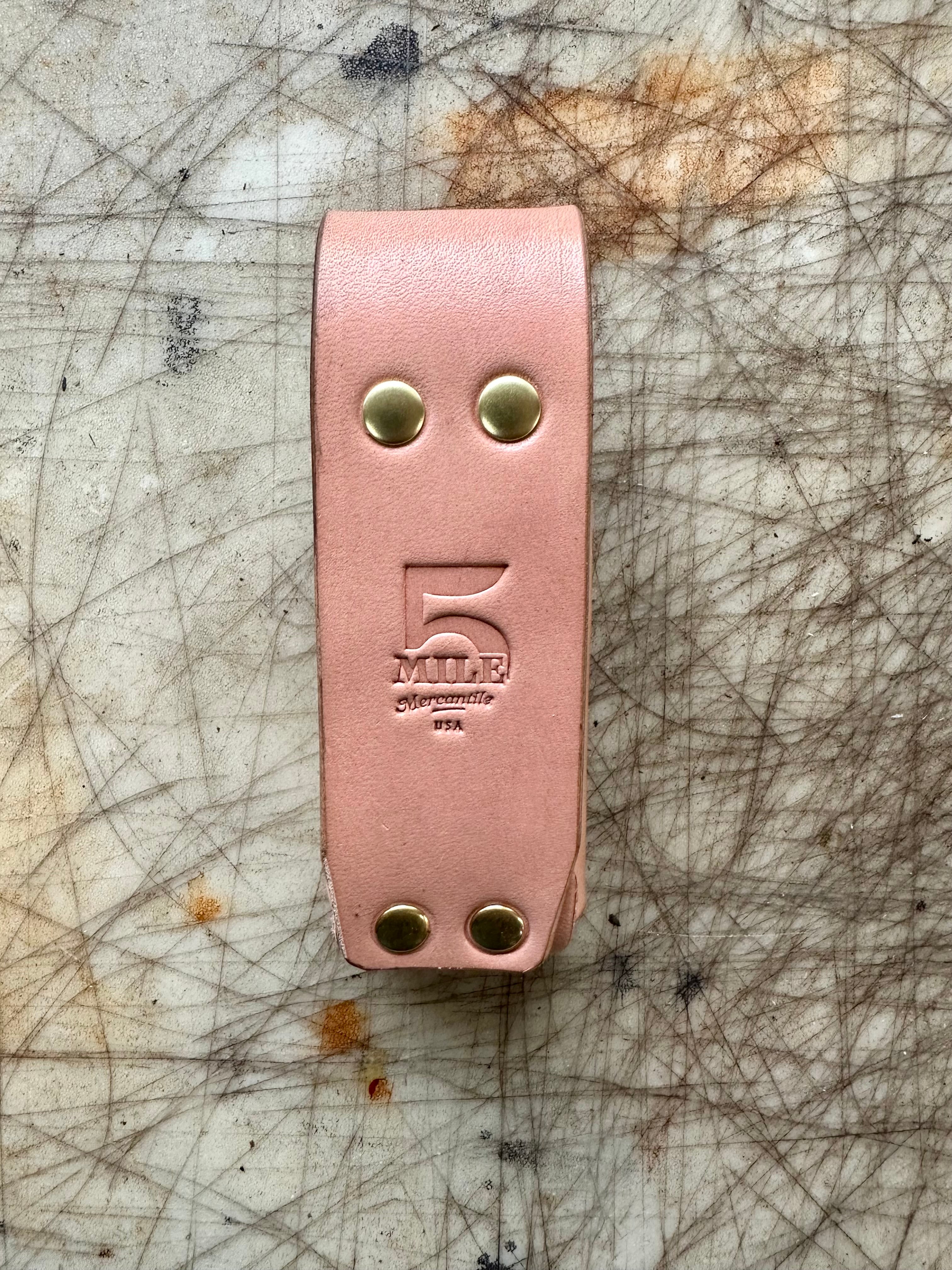 Pink leather strap with gold hardware on a scratched surface