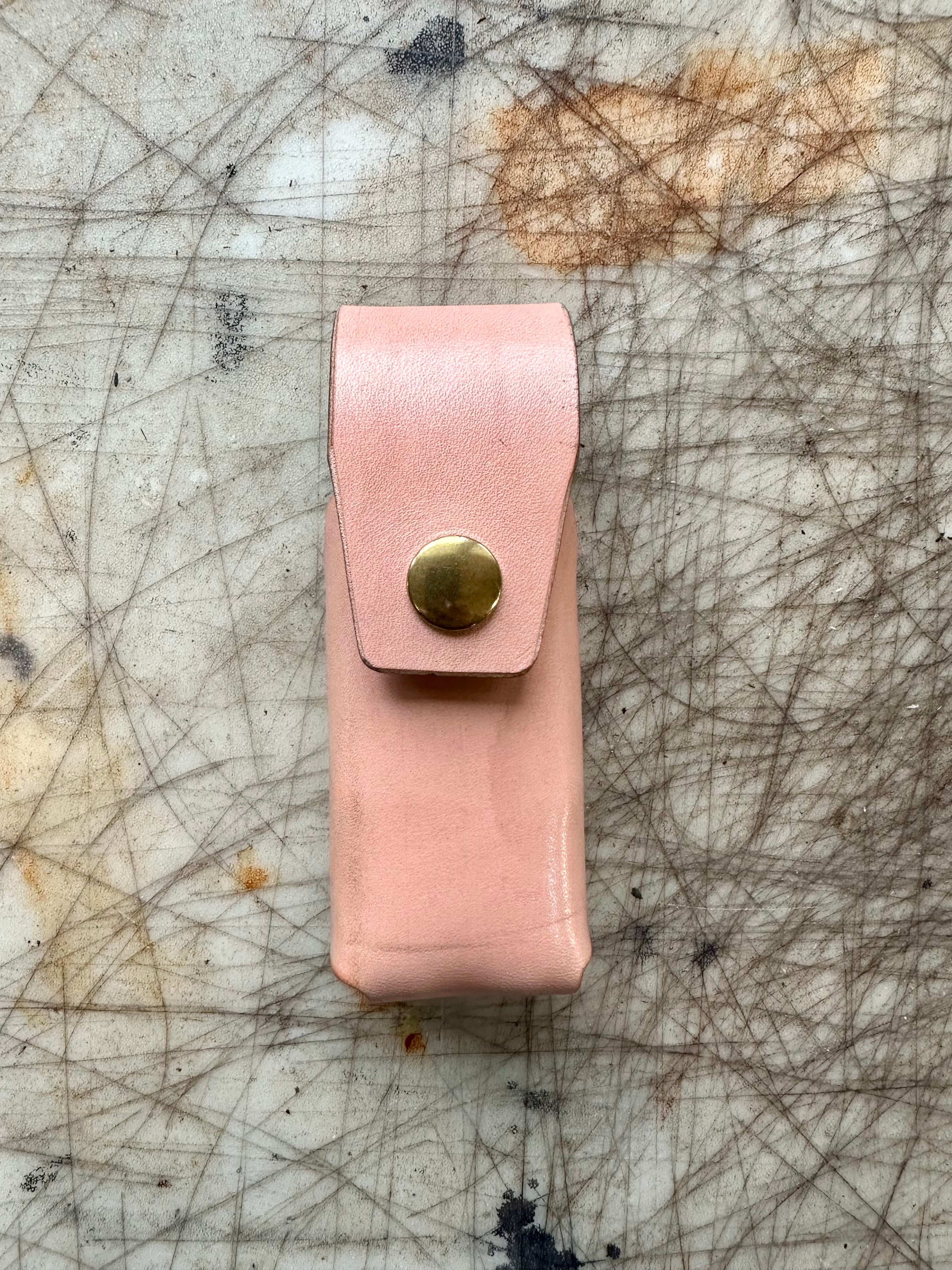 Pink leather pouch with a gold button on a textured surface