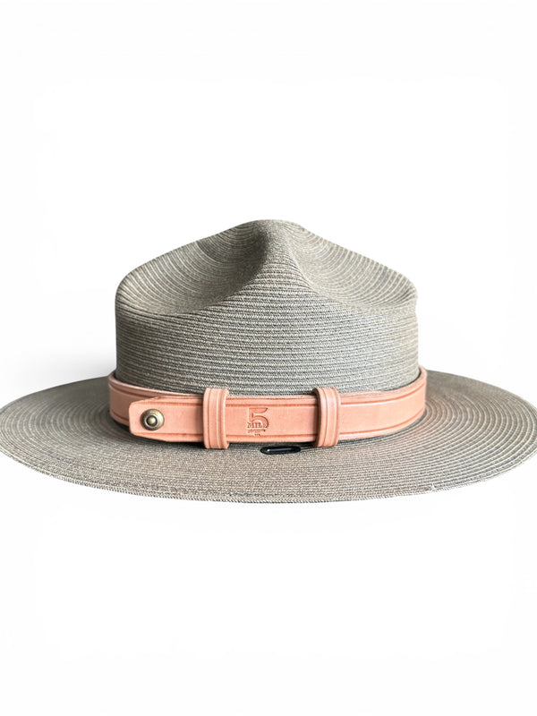 A light gray woven wide-brim hat with a dusty pink leather band and buckle closure, shown against a plain white background.