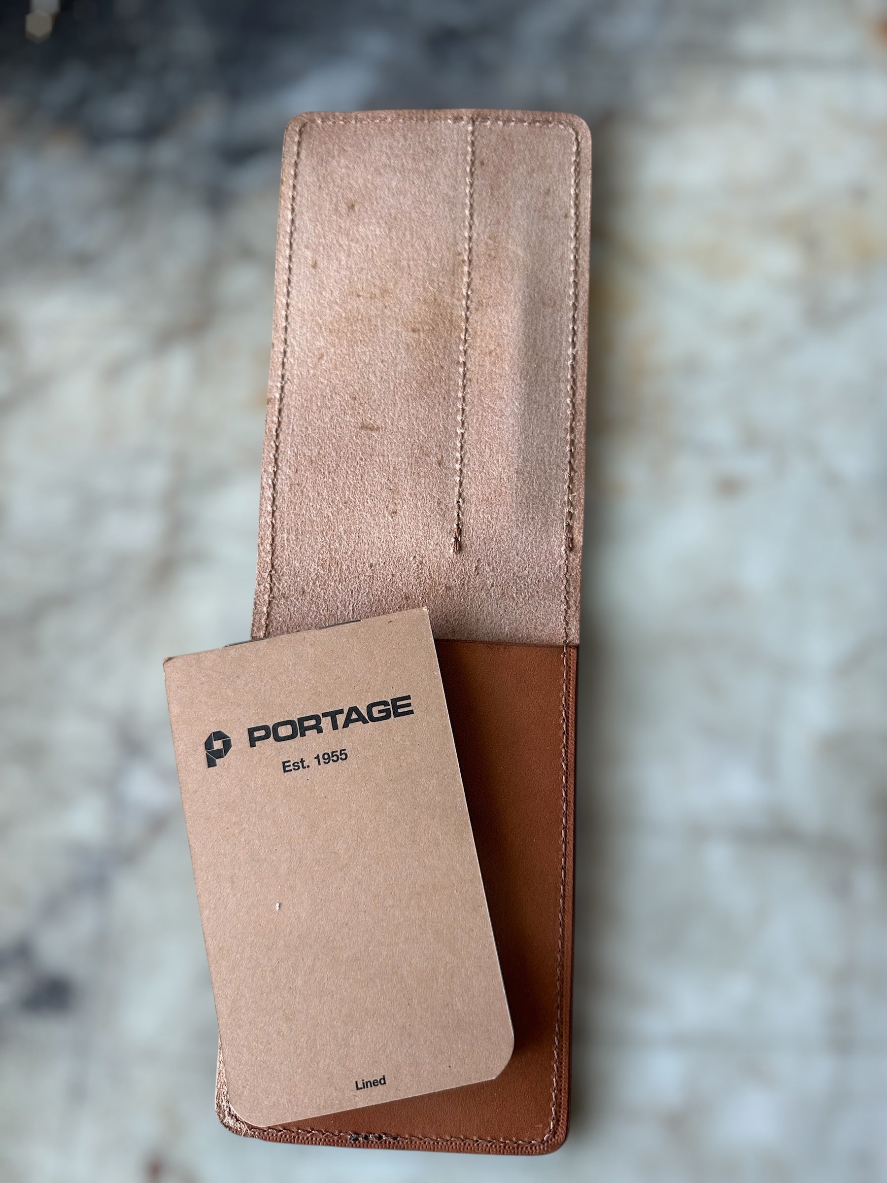 Brown leather pouch with a smaller brown card inside, on a marble surface.