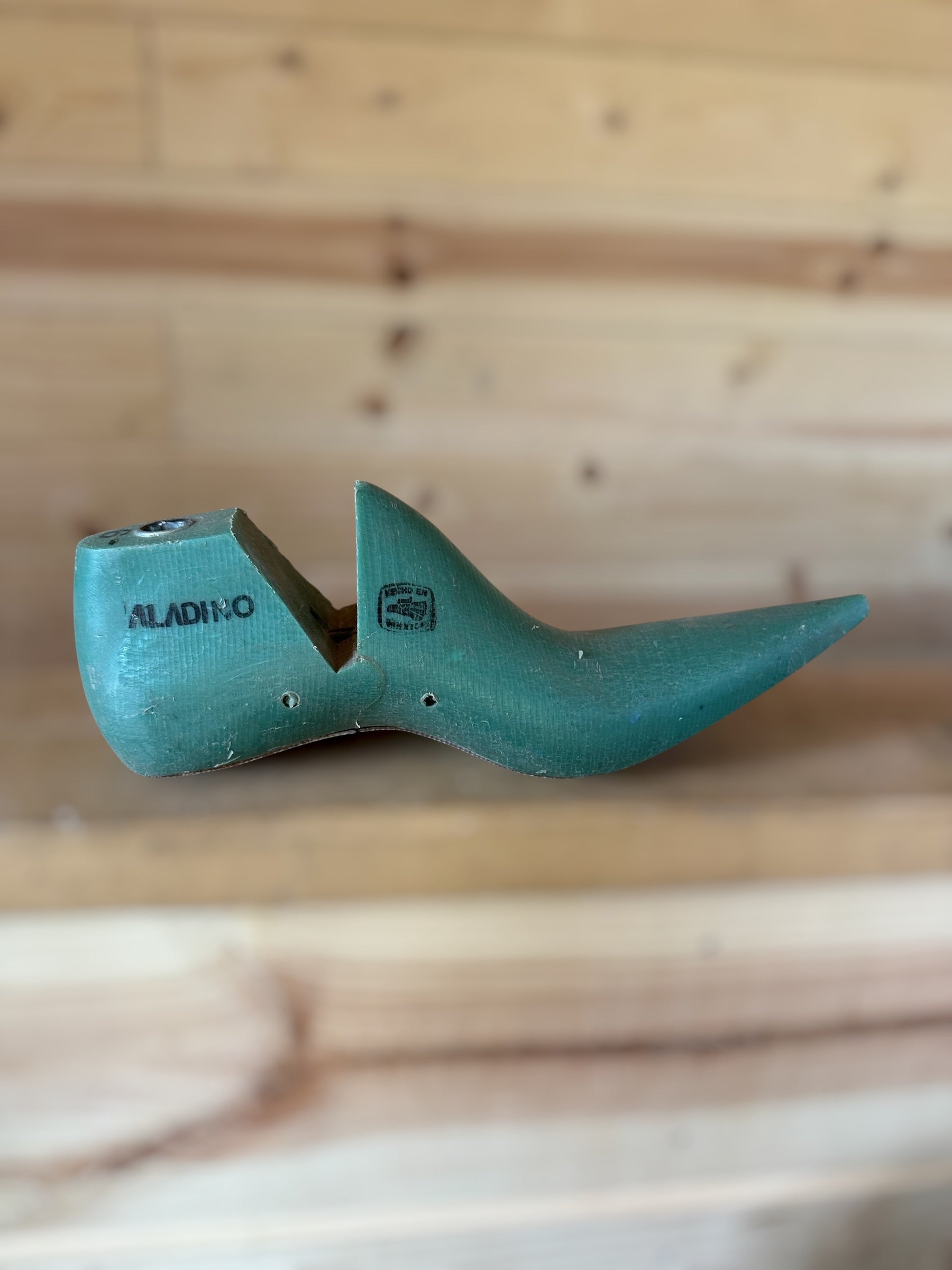 A vintage teal green shoe tree with the brand name 'ALADINO' printed on the side, resting on a light-colored wooden plank surface.