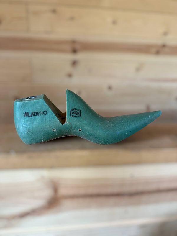A vintage teal green shoe tree with the brand name 'ALADINO' printed on the side, resting on a light-colored wooden plank surface.