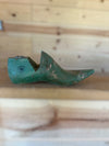 A vintage green wooden shoe tree with a weathered, distressed finish, resting on a wooden surface against a light wood plank background.