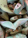 A close-up pile of vintage wooden shoe lasts in a distressed sage green finish, with some showing natural wood grain and stamped letter markings.