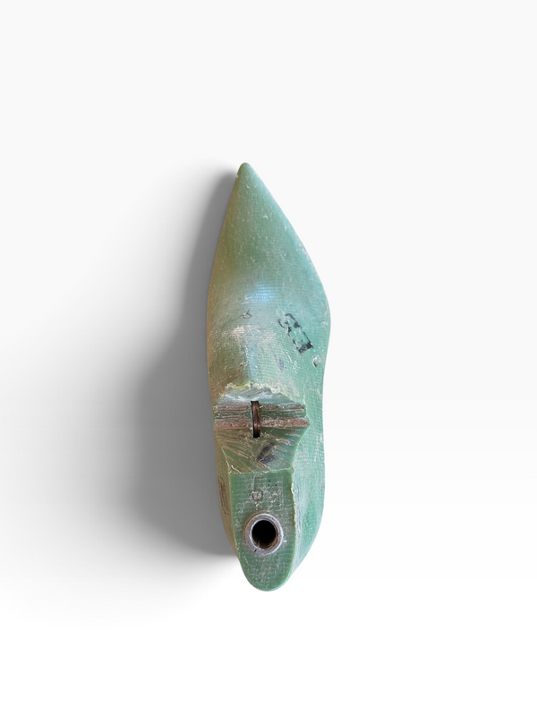 A small pointed green ceramic object with a circular hole at the base and a small metallic loop near the center, photographed against a plain white background with a soft shadow.