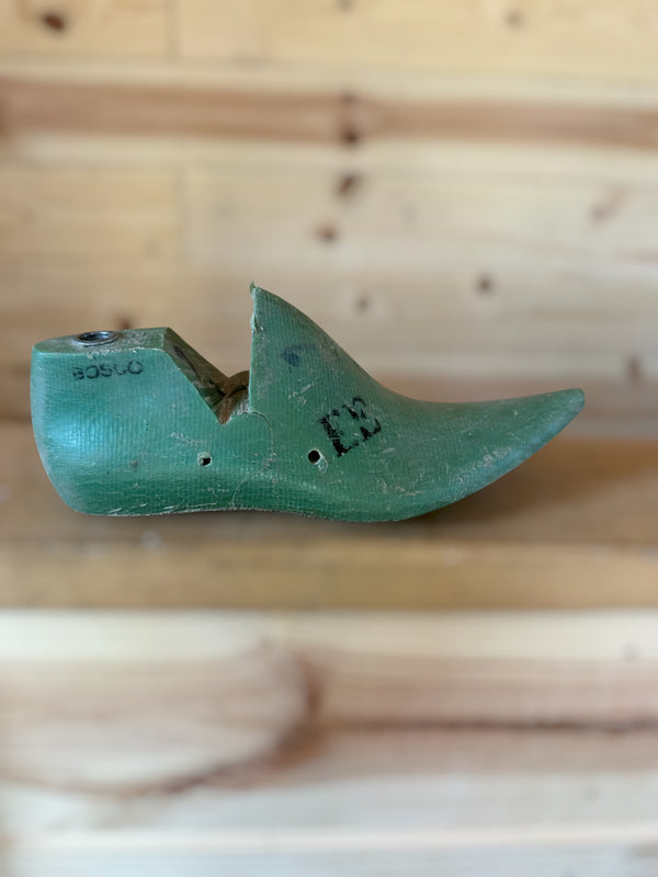 A vintage green wooden shoe tree with black printed numbers, resting on a light wood surface against a wooden background.