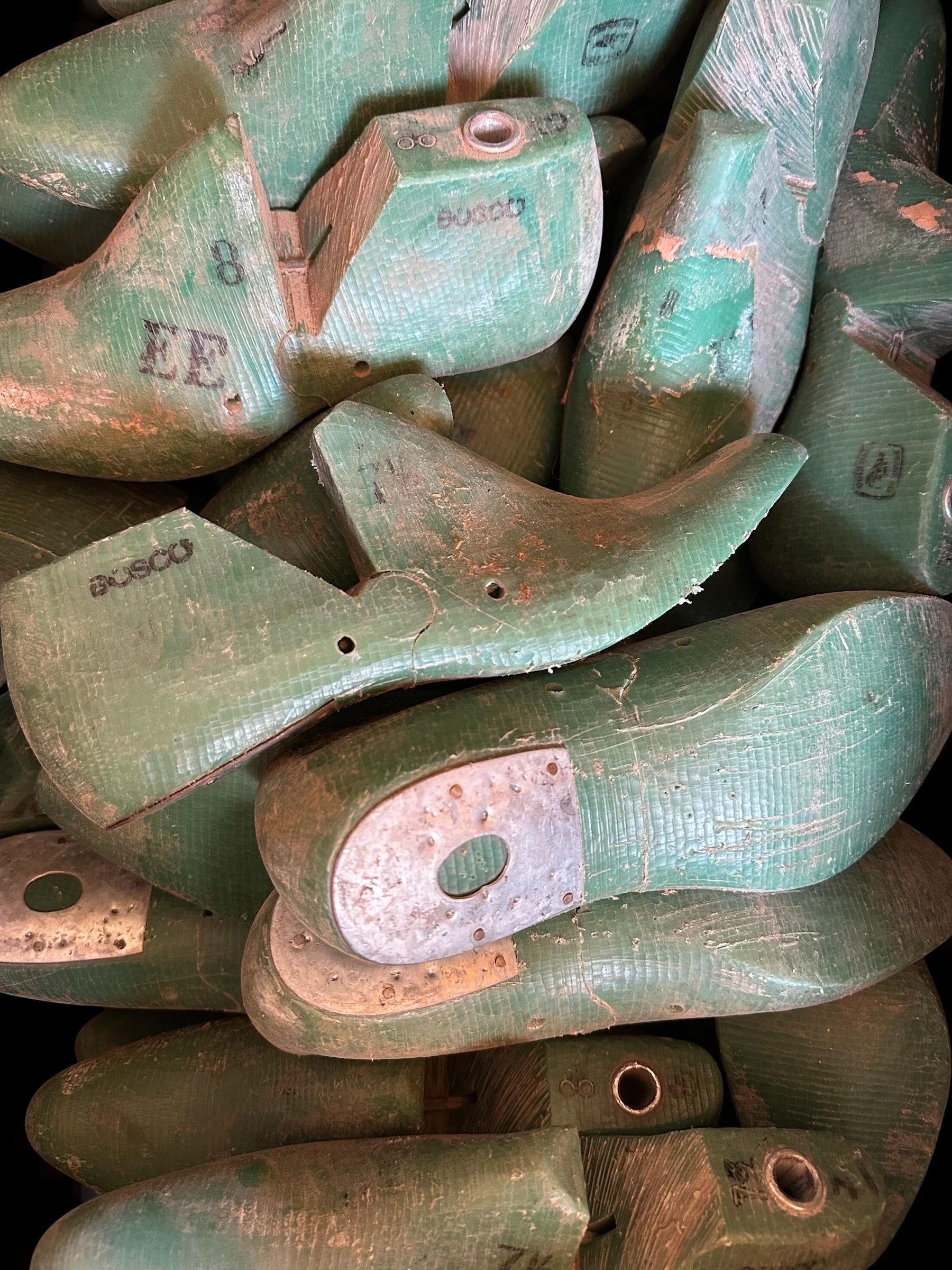 A close-up pile of vintage green wooden shoe lasts, some showing the brand name 'BOSCO' and others with worn, weathered surfaces.