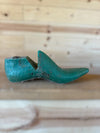 A vintage wooden shoe tree with a distressed teal-green painted finish, resting on a light wood plank surface against a matching wooden background.