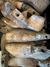 A close-up pile of vintage wooden shoe lasts, showing weathered brown wood with white handwritten numbers on some pieces.