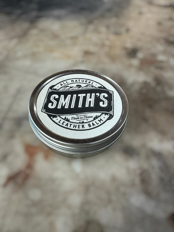 A round metal tin of Smith's Leather Balm with a white and black label, resting on a blurred stone surface.