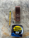 Stanley tape measure, leather strap, and pencil on a scratched surface
