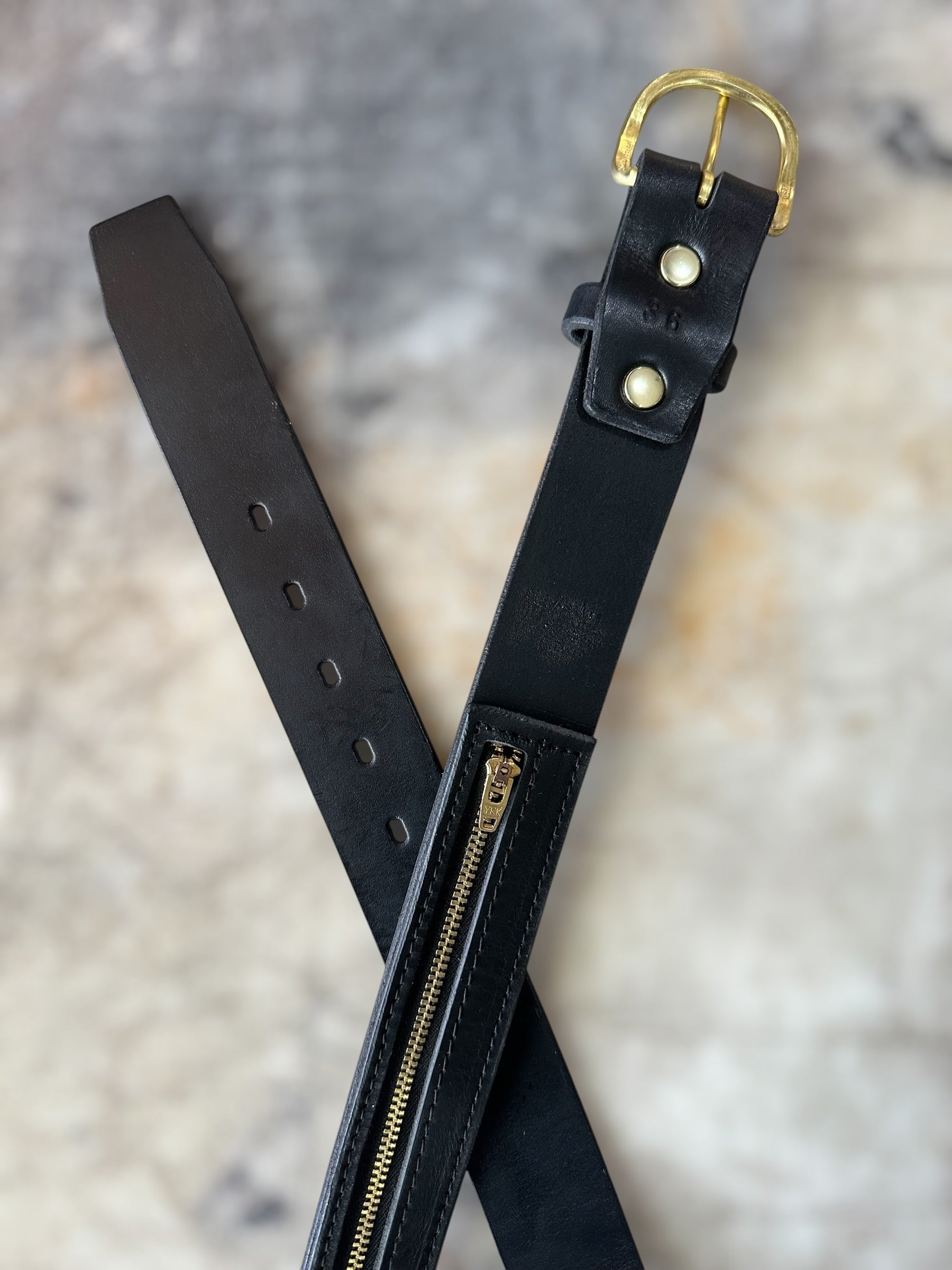 Black leather belt with gold buckle and zipper on a textured surface