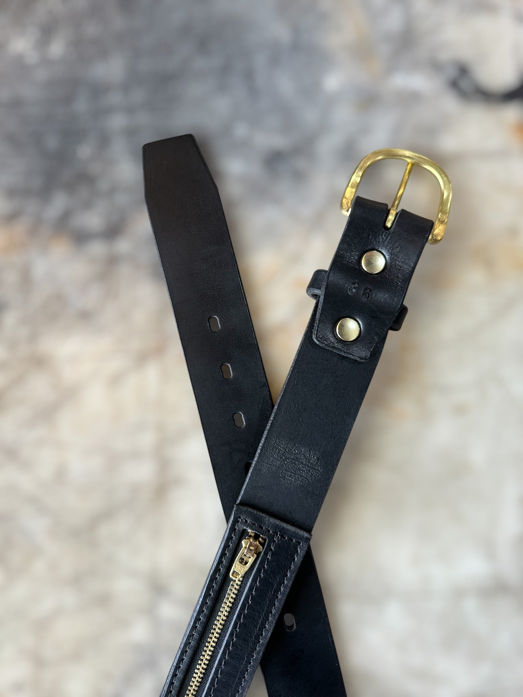 Black leather belt with gold hardware on a textured surface