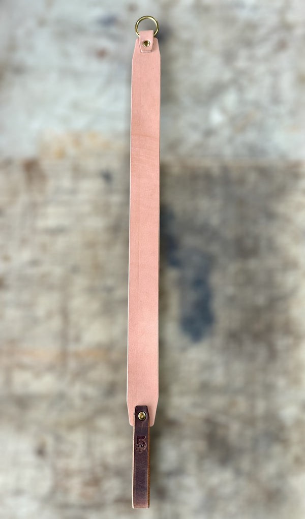 Long pink leather strap with a gold ring on a textured gray background