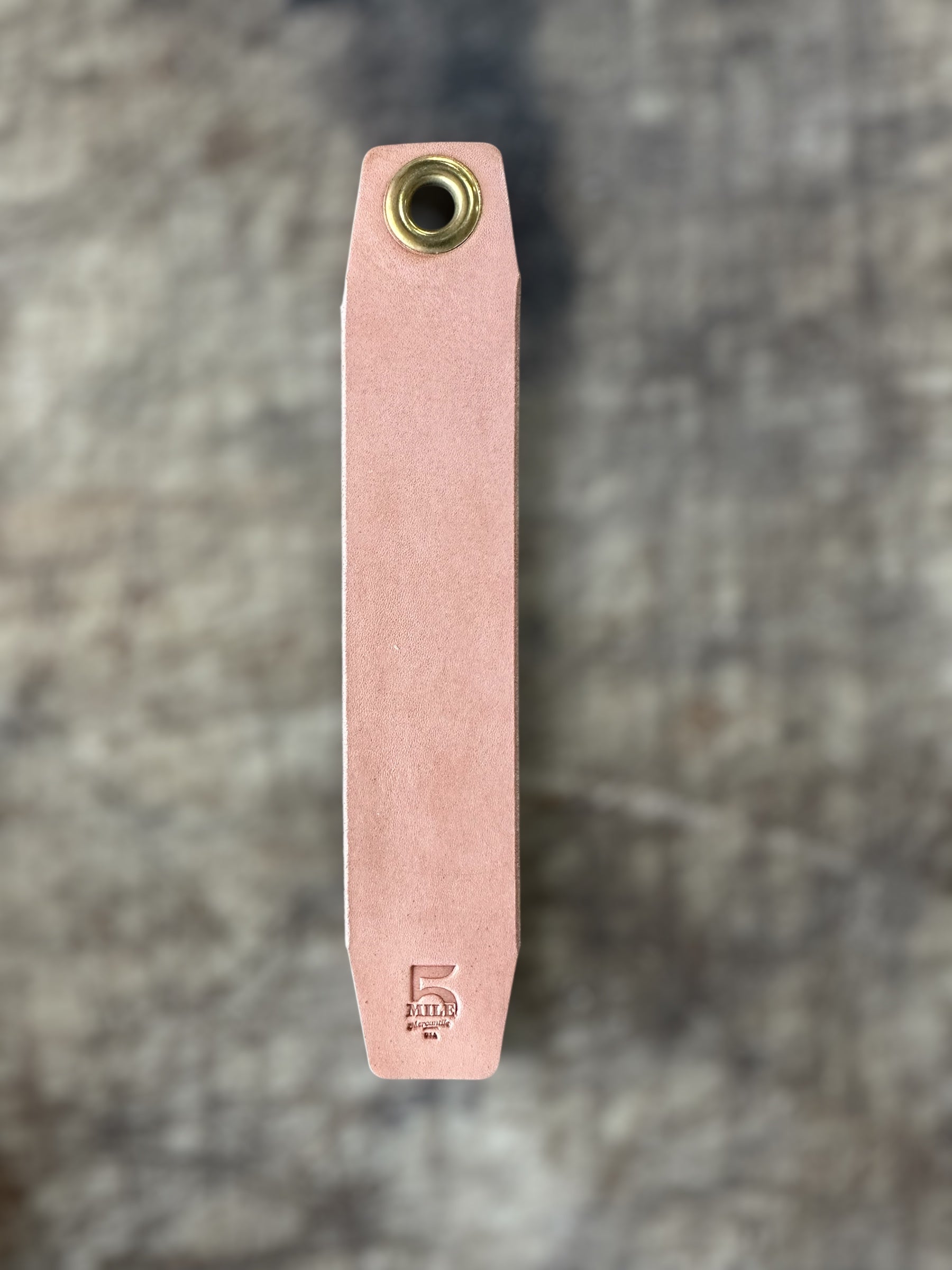 Pink leather tool with brass fitting on a textured gray background