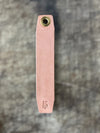 Pink leather tool with brass fitting on a textured gray background