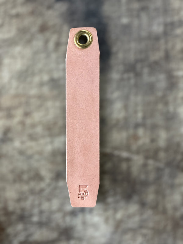 Pink leather tool with brass fitting on a textured gray background