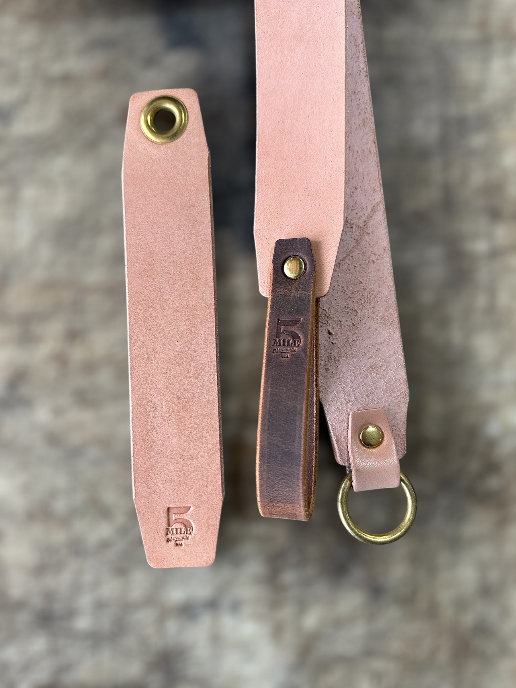 Two leather straps with brass hardware on a textured surface