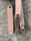 Two leather straps with brass hardware on a textured surface