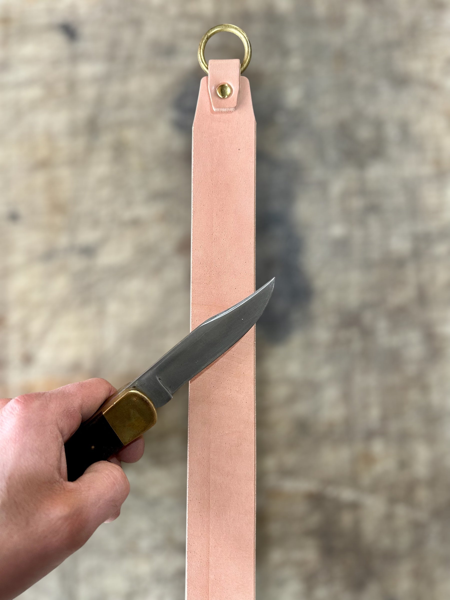 Knife with a pink leather sheath held by a hand against a neutral background