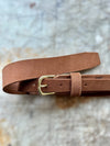 Brown leather belt with a gold buckle on a textured surface