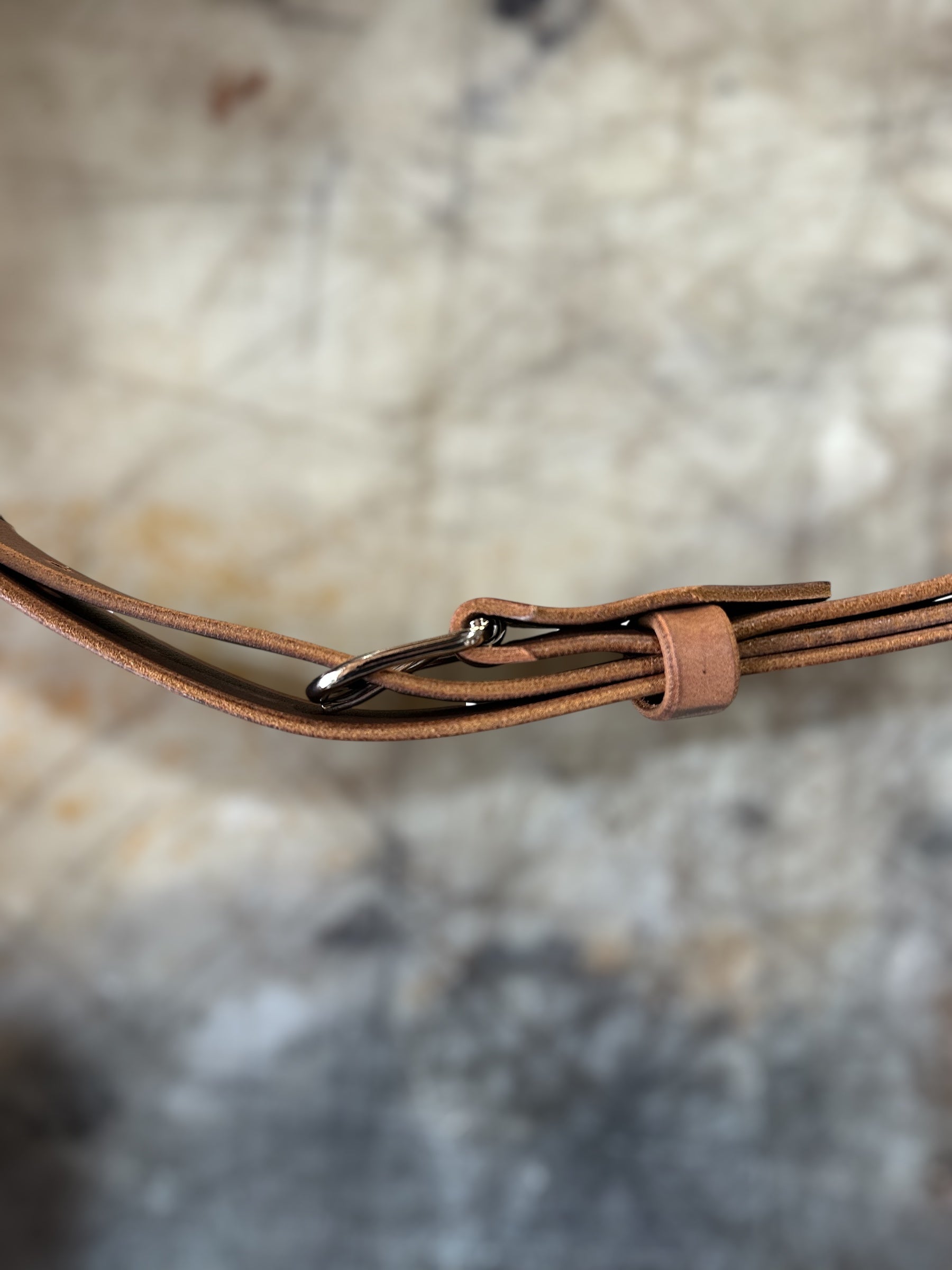 Close-up of a brown leather strap with a buckle on a textured beige background