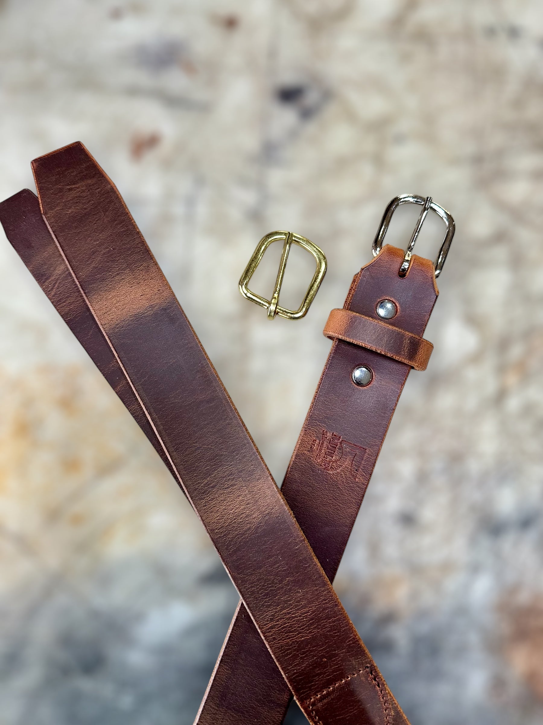 Brown leather belt with gold and silver buckles on a textured surface