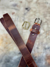 Brown leather belt with gold and silver buckles on a textured surface