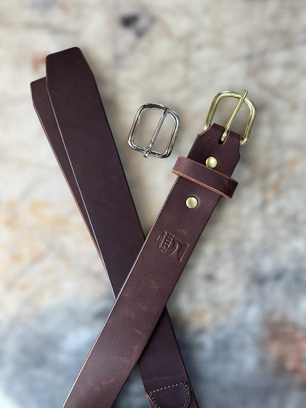 Brown leather belt with gold and silver buckles on a textured surface