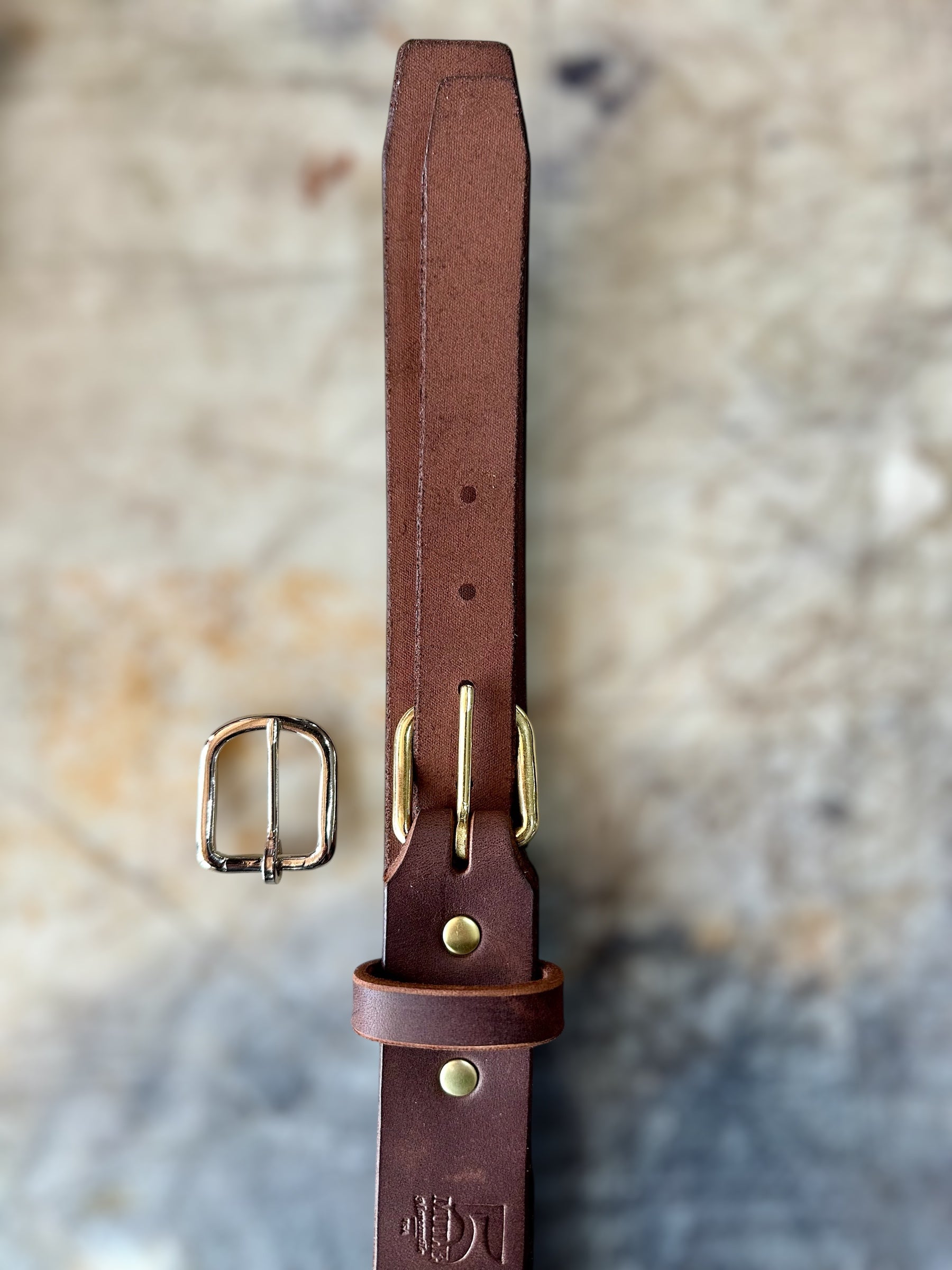 Brown leather belt with brass buckle on a textured stone background