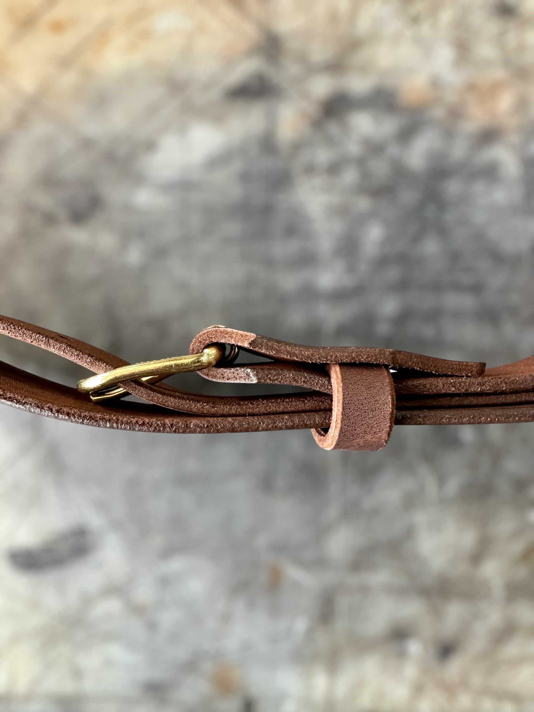Close-up of a brown leather strap with a gold buckle on a stone surface