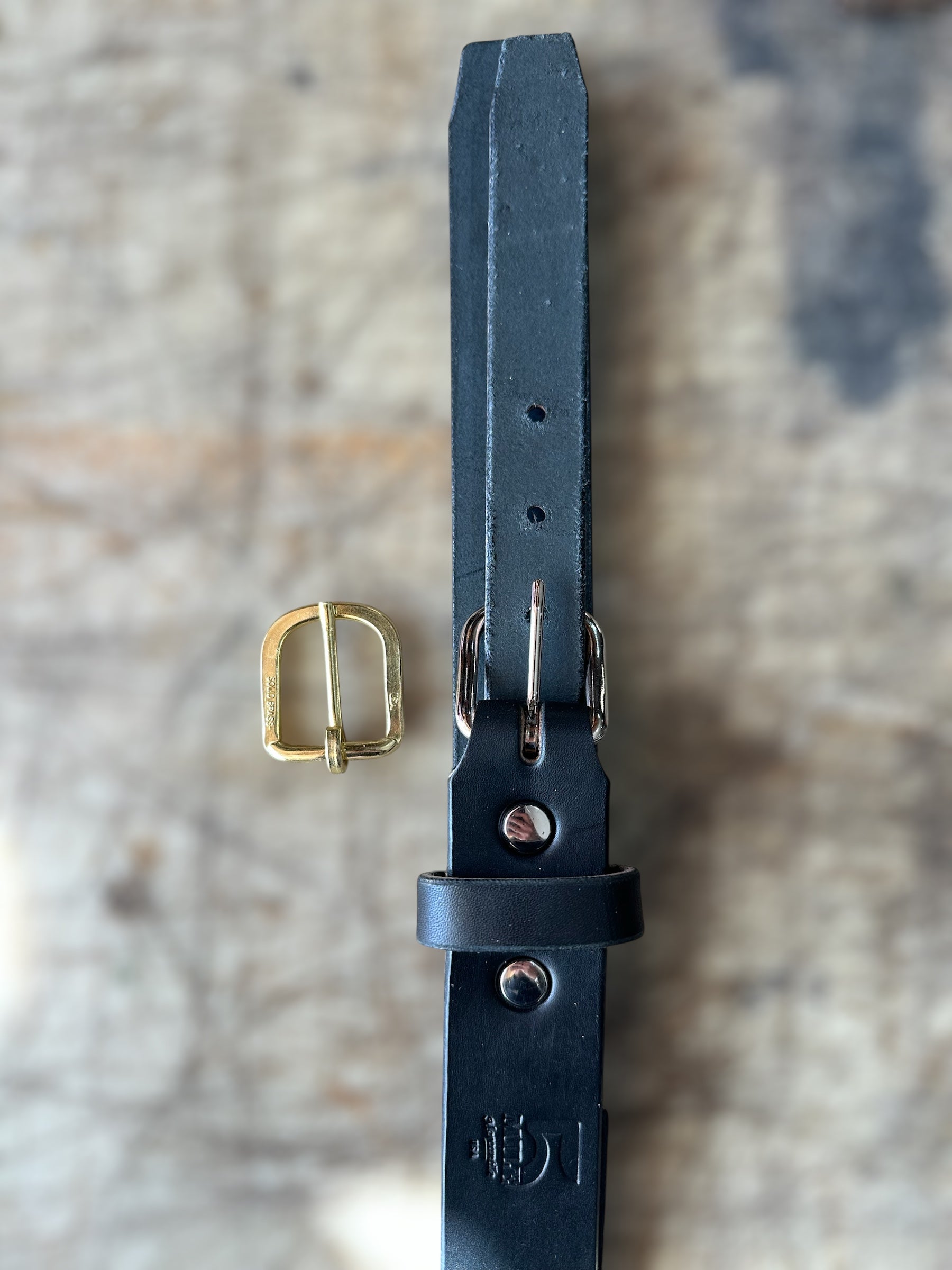 Black leather belt with gold buckle on a textured surface