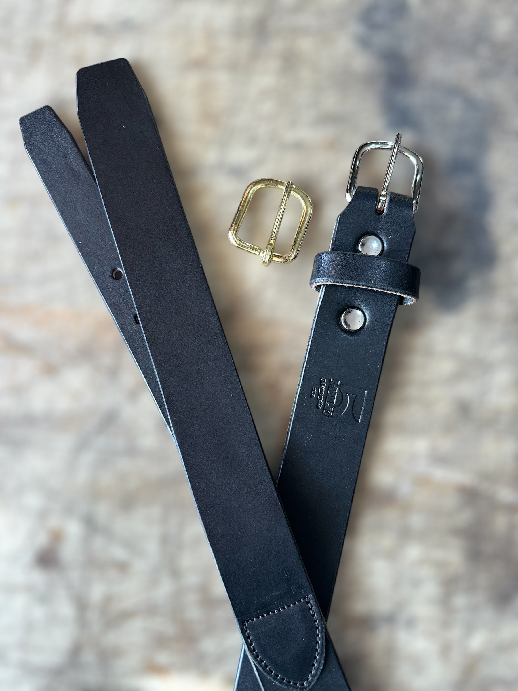 Black leather belt with gold and silver buckles on a textured surface