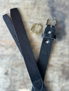 Black leather belt with gold and silver buckles on a textured surface