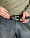Person adjusting a black belt with a brass buckle on gray pants.
