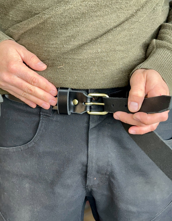 Person adjusting a black belt with a brass buckle on gray pants.